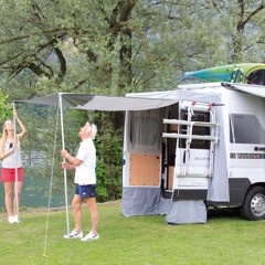 Campervan med uppsatt tält och markis, uppsatt av två personer i naturen.